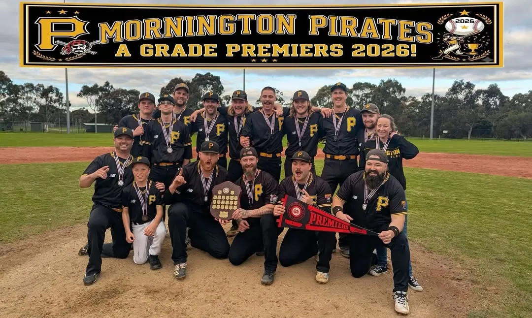 The 2026 A1 premiers on the mound in their medals, with the premiership shield and a Premiers pennant, under a banner reading “Mornington Pirates A Grade Premiers 2026!”
